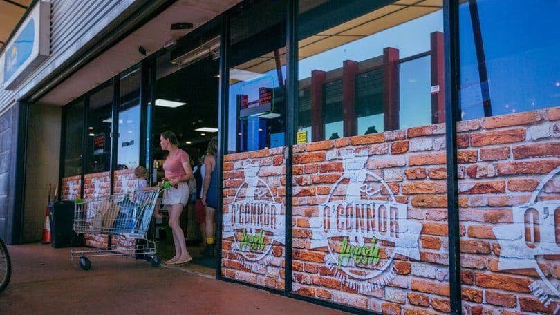 Woman pushing a shopping cart while exiting the O’Conner Fresh Store